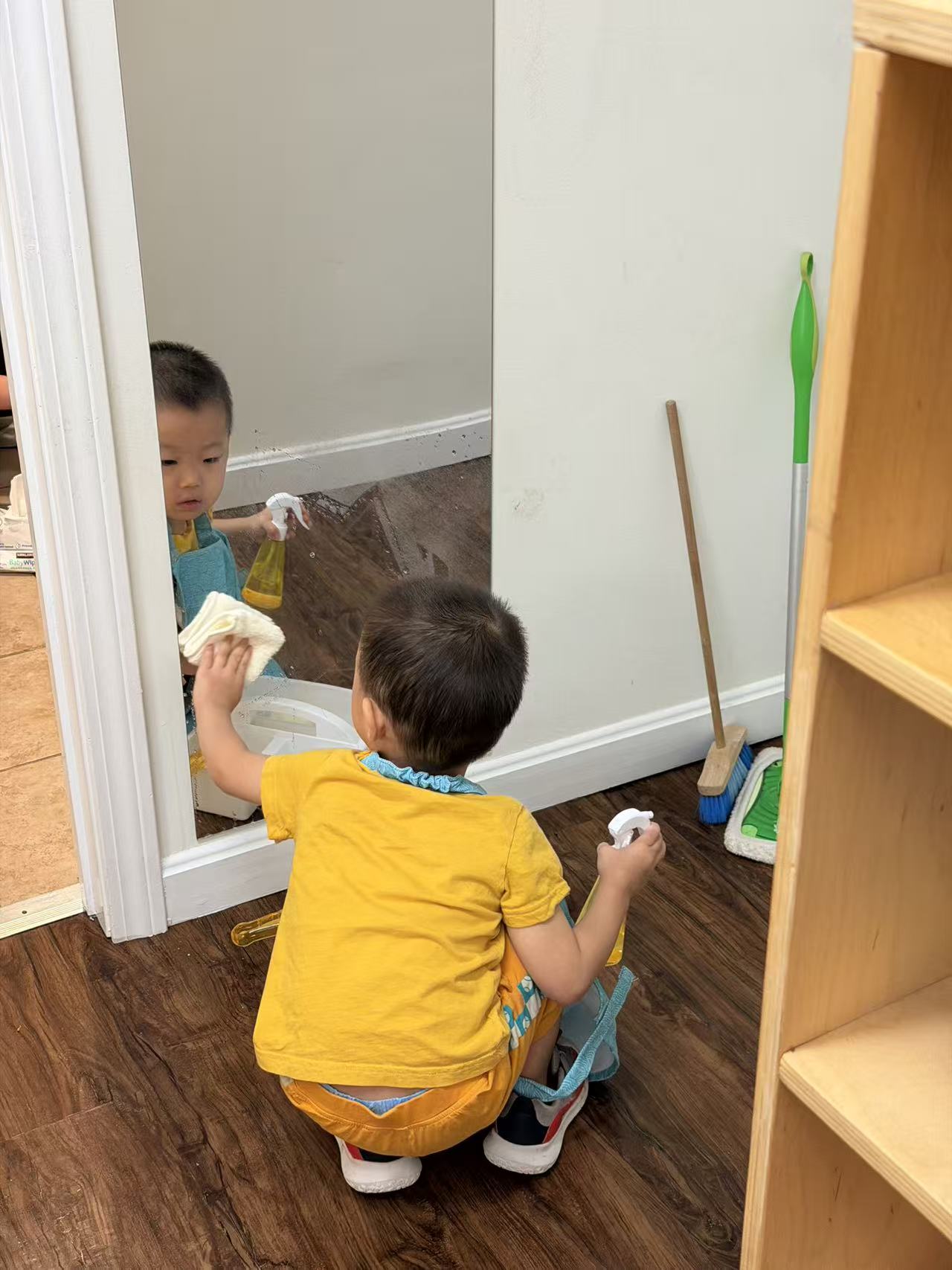 a child spraying and wiping a mirror clean